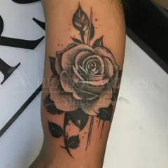 A large, beautifully shaded black and grey rose tattoo on the forearm, showcasing detailed petal work.