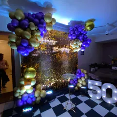 This vibrant 50th birthday photo booth combines a gold sequin wall with a "Happy Birthday" neon sign and large marquee numbers. The purple and gold balloons add a fun and celebratory finishing touch.