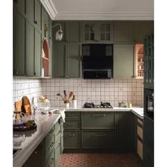 A full view of the olive green kitchen, showcasing the terracotta floor tiles and hand-painted backsplash. The layout is designed for easy workflow, with an arched niche providing a connection to the dining area.