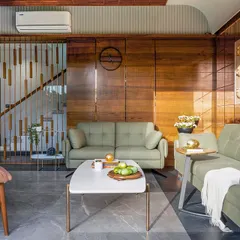 This wider view of the living space at Tranquil Mango Haven showcases the holistic spatial planning. The slatted wooden screen provides a subtle division for the staircase while maintaining an open feel, and the furniture is arranged to encourage both social connection and quiet reflection.