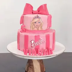 Hi Barbie. I finally got to make a cake for the Barbie trend. This two-tier pink cake features stripes, an edible image of Barbie, and a large, handcrafted fondant bow on top.