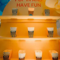 A "Pop in and have fun" popcorn station at a carnival-themed party. The custom-built yellow shelf is designed to hold individual popcorn boxes for guests.