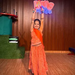 Dressed in a vibrant orange bandhani lehenga, this student holds her dandiya sticks high. This photo highlights the colorful and festive atmosphere of our Navratri dance workshops.