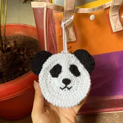 A hand holding the crochet panda pouch, giving a sense of its size and soft texture.
