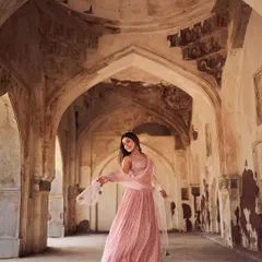 A wide-angle shot capturing the grandeur of the location and the elegance of the pink lehenga. The architectural arches frame the model, creating a sense of scale and romance for this ethnic wear campaign.