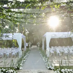 An outdoor ceremony setup with elegant white canopies and a flower-lined aisle, bathed in beautiful sunlight.
