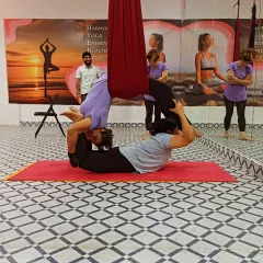 A complex Acro Yoga pose where the flyer performs a deep backbend while balanced on the base's feet, with the aerial hammock providing an extra layer of support. I am spotting to ensure everyone's safety.