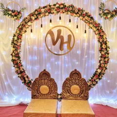 I designed this elegant engagement stage with a large floral ring of artificial roses, warm Edison bulb lighting, and a custom gold monogram for the couple. The traditional chairs complete this beautiful setup for a ring ceremony.