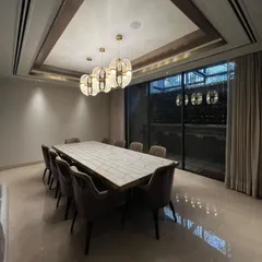 This dining room blends modern forms with Art Deco elegance. A large, minimalist dining table is surrounded by plush, comfortable chairs, while a series of geometric, Art Deco inspired chandeliers with gold accents provide a dramatic focal point.