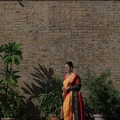 A full-length portrait of a Maharashtrian bride against a textured stone wall, the play of light and shadow adding an artistic, dramatic touch.