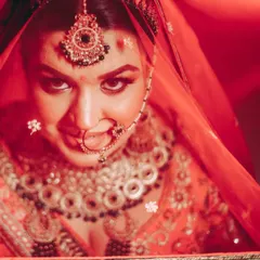 A captivating close-up of a bride under her red veil, looking directly at the camera. The intense red lighting and her expression create a powerful and dramatic portrait.