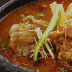 A close-up of a rich and aromatic mutton curry. The tender meat, slow-cooked in a blend of traditional spices and garnished with fresh ginger and chili, represents the heart of North Indian fare that inspires our menus.