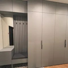 This modular wardrobe unit in Gurgaon includes a built-in entryway bench with a cushioned seat and coat hooks. The floor-to-ceiling design in a matte grey finish maximizes storage and adds a functional feature to the room.