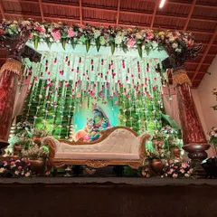 A beautiful baby shower stage featuring a Krishna and Yashoda backdrop, surrounded by hanging floral decorations and traditional pillars.