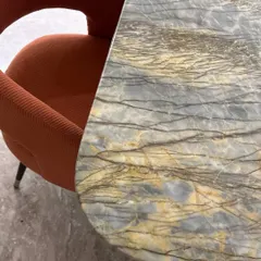 A close-up showcasing the beautiful combination of materials: a vibrant orange corduroy armchair next to a stunning marble tabletop with intricate grey and gold veining.