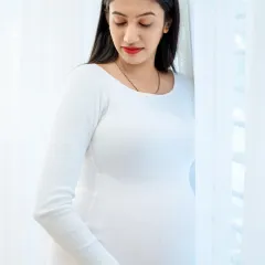 A serene solo portrait of the mother-to-be by the window. The soft, natural light and the simple white dress create a timeless and elegant image.