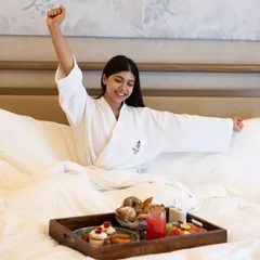 A woman stretches happily while enjoying breakfast in bed. Our resort is the perfect place for a self-care getaway, offering serene moments of relaxation and rejuvenation.