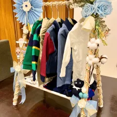 A unique and creative presentation for a baby boy's gift hamper. We have arranged a selection of high-quality baby clothes on a miniature decorative clothing rack, adorned with blue floral accents and delicate ribbons.