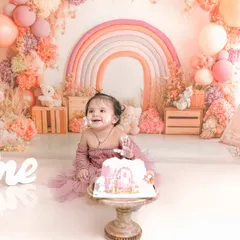 A happy, cake covered smile during a first birthday cake smash. The setup features a boho rainbow arch, a miniature teepee, and soft pastel balloons.