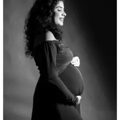 A joyful black and white solo portrait. The side lighting beautifully highlights the mother-to-be's smile and baby bump.