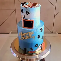 A special cake for a teacher's 75th birthday. This two-tier Swiss Chocolate cake has a blue ombre design and is decorated with fondant books, a chalkboard, and other school-themed items.