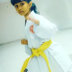A young girl in a yellow belt holds a strong fighting stance. We empower our students with the confidence that comes from mastering fundamental karate postures.