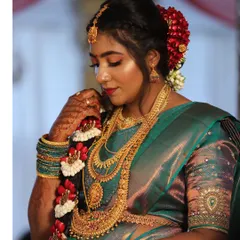 A side profile showcasing the complete South Indian bridal attire. The makeup is balanced to harmonize with the heavy gold necklaces and the traditional floral hair braid, ensuring a cohesive and elegant look.