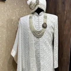 A classic white-on-white embroidered sherwani. This piece is designed for a sophisticated and clean look, complete with a matching turban and a layered pearl necklace for a touch of royalty.