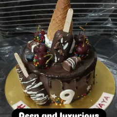 An overloaded chocolate drip cake. This indulgent creation is topped with mini cakesicles, an ice cream cone, fresh cherries, and colorful sprinkles.