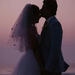 A romantic silhouette of the bride and groom against a purple twilight sky. The groom's kiss on her forehead is a tender and timeless gesture.