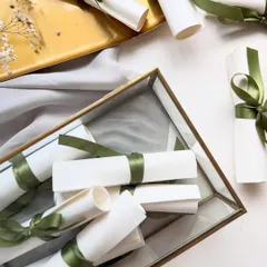 A collection of handwritten wedding vows, rolled into scrolls and tied with green silk ribbon. They can be presented in a beautiful glass box as a lasting memento of the wedding day.