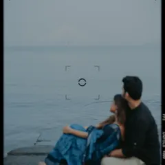 An atmospheric shot of the couple by the sea, with the Bandra-Worli Sea Link faintly visible, framed like a vintage film still.