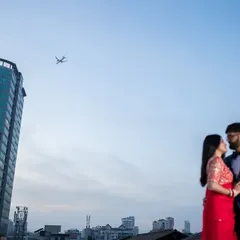 A wide, cinematic frame capturing the couple against the city skyline, with a plane flying overhead. This shot adds a layer of storytelling, suggesting travel, destiny, and a love story in a modern world.