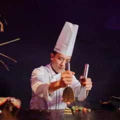 A chef showcases his teppanyaki skills at a live station, engaging guests with precision and flair. This is a perfect entertainment addition for corporate events.