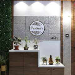 An entrance foyer designed with a mix of textures, including a green wall, wood paneling, and silver textured panels. A custom nameplate and a multi-level shoe cabinet with display niches create a functional and stylish entry.
