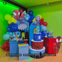 A multi-level Spider-Verse party setup, complete with themed pedestals for cake and treats, character cutouts of different Spider-heroes, and a city backdrop.