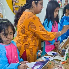 I love guiding my students as they learn new techniques. Here, I'm helping a young artist with color blending on her canvas, ensuring she feels confident and supported.