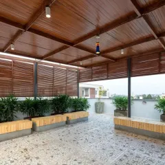 A spacious rooftop terrace designed as an outdoor lounge. The space features a wooden pergola for shade, built-in benches, and planters with easy-to-maintain greenery.