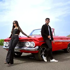 A full-shot of the couple posing with a vibrant red vintage car, showcasing a cool, editorial style for a pre-wedding photoshoot.
