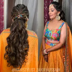 A fun and festive ponytail for a Mehendi ceremony, featuring a braided crown and colorful bead accessories. The soft waves add a playful touch to this vibrant look.