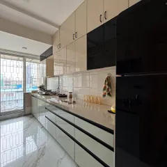A wider angle of the parallel kitchen layout, showing the dual-tone cabinet design in cream and black. The marble-patterned flooring adds a touch of luxury.