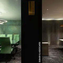 A view into two distinct yet connected spaces. On the left, a conference room with vibrant green chairs against a textured wall, and on the right, an executive office with warm wood paneling, showcasing our ability to create varied moods within a cohesive design.