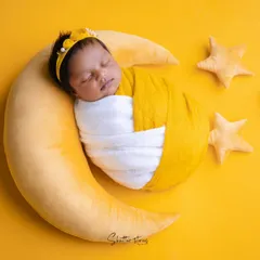 Over the moon for this little one. Inspired by a mango softy, this setup features a baby swaddled in yellow and white, sleeping peacefully on a crescent moon prop with little stars.
