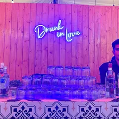 Two of our bartenders ready for a wedding party behind a custom bar. The "Drunk in Love" neon sign adds a fun, romantic touch to the setup.