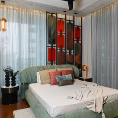 This wider view of the master bedroom shows how the sheer drapes soften the natural light, creating a serene and airy atmosphere. The pendant lights add a touch of understated luxury and warmth.