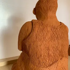 A back view of the seated woman sculpture, showing the intricate texture work on her clothing. Every mark is made by hand, adding to the piece's unique character.