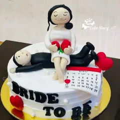A playful 'Bride to Be' cake for a bachelorette party or bridal shower. The handcrafted fondant figures show the bride-to-be relaxing while her groom lies down, with a calendar marking the big day.