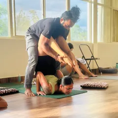 An instructor providing a deep adjustment in an advanced inversion. This level of guided assistance helps a student safely explore the limits of their flexibility and strength.