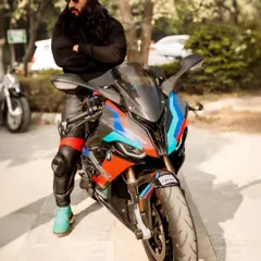 A full-body shot showing the rider's complete gear and the striking design of the BMW S1000RR. The pose is confident and cool.
