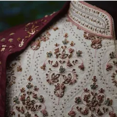 A close-up view of the fine craftsmanship on one of our sherwanis. This shows the detailed threadwork and sequin embroidery in multiple colors on an off-white base fabric, paired with a rich maroon stole.